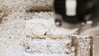 Nahaufnahme einer gefrästen Brillenfassung, die in Spänen und -staub eingebettet ist. Ein Teil der Fräsmaschine ist zu sehen.