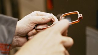 Nahaufnahme von zwei Händen, die ein braun-transparentes Brillengestell halten. Mit der rechten Hand wird die Brille geschliffen, während die andere Hand das Gestell dreht.